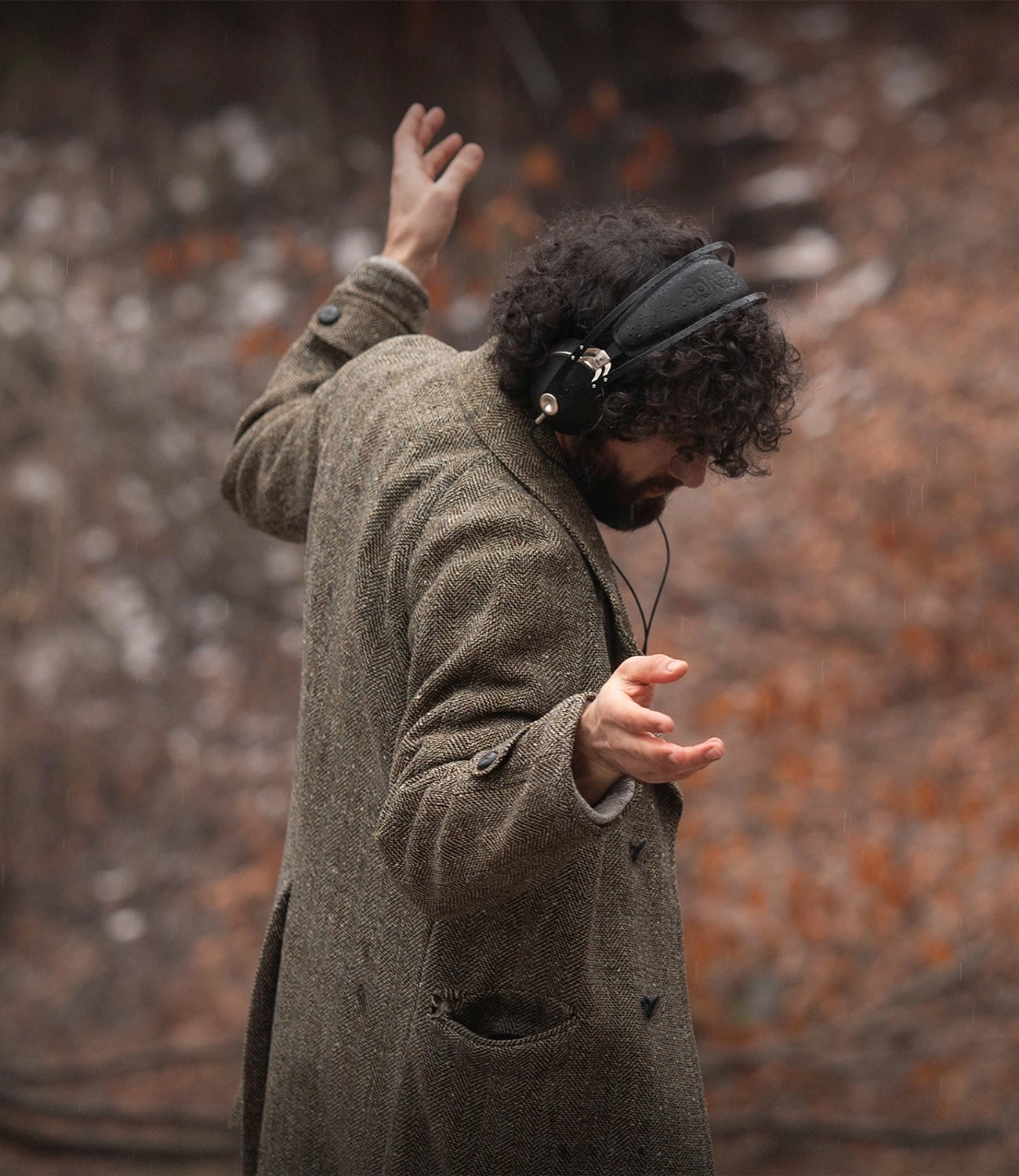 Man in overcoat walking in the forest dancing and listening to music on his Meze Audio 99 NEO wired head phones