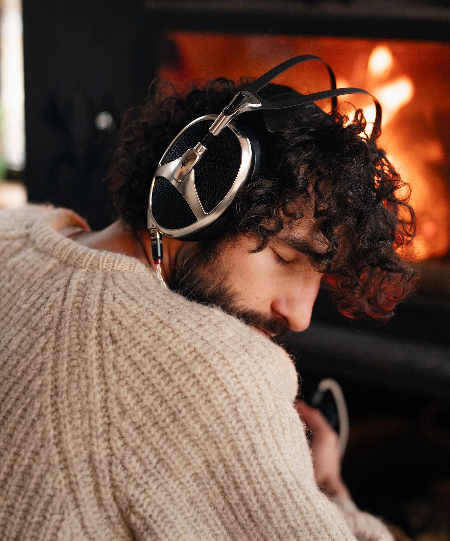 Man sitting next to cozy fireplace with closed eyes listening to music on his Meze Audio Elite planar wired head phones