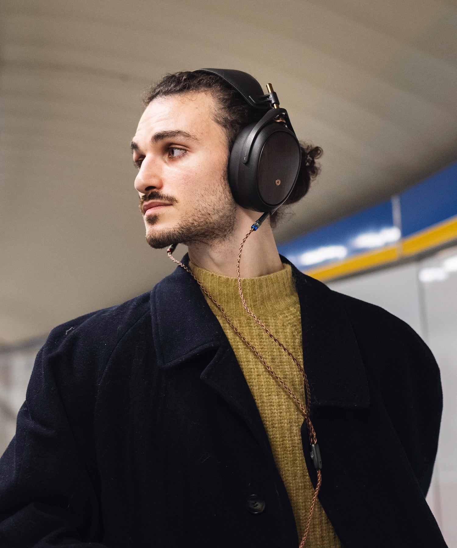 Man in overcoat glancing at his surroundings while traveling and listening to music on his Meze Audio LIRIC wired head phones
