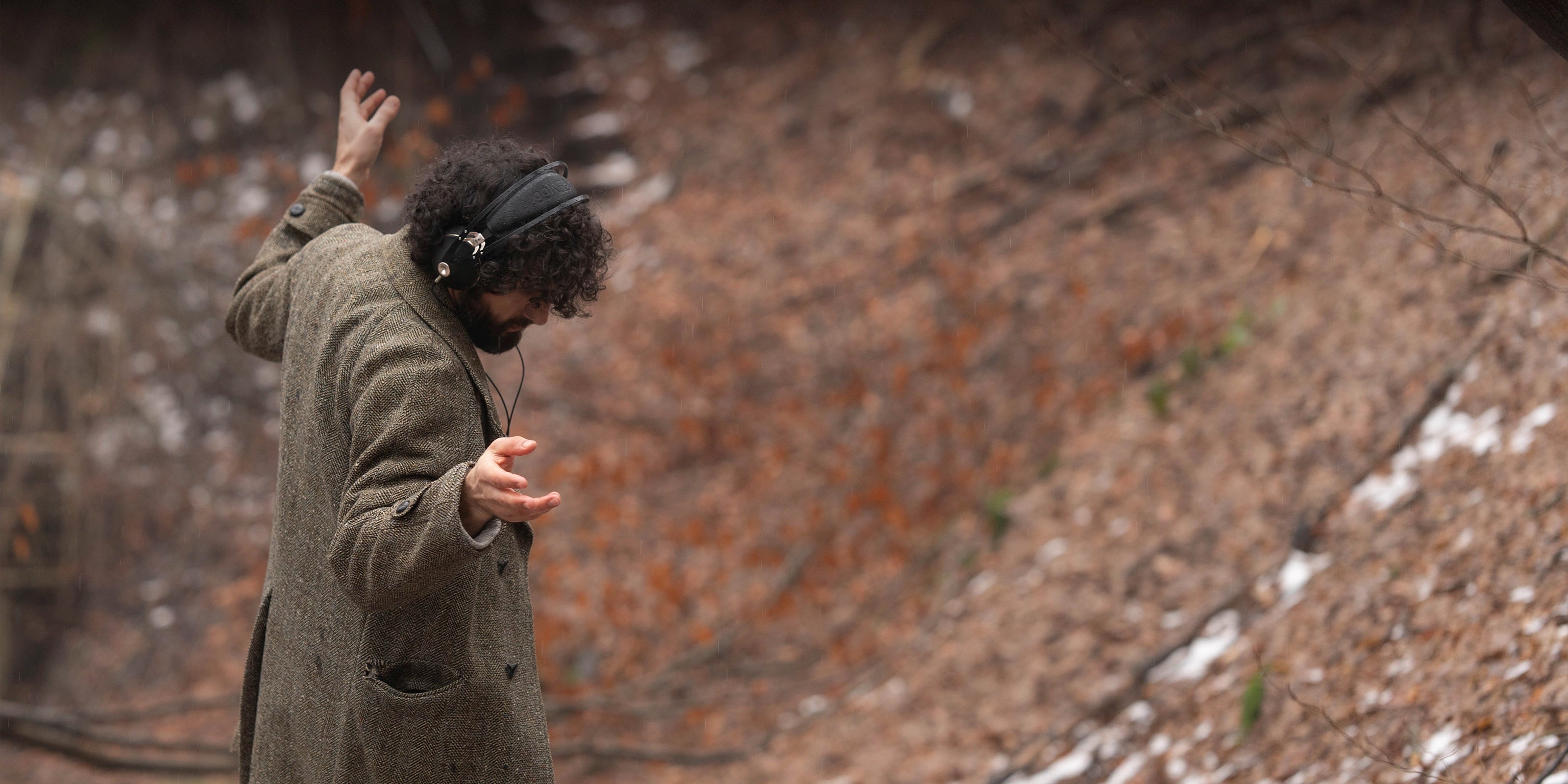 Man in overcoat walking in the forest dancing and listening to music on his Meze Audio 99 NEO wired head phones