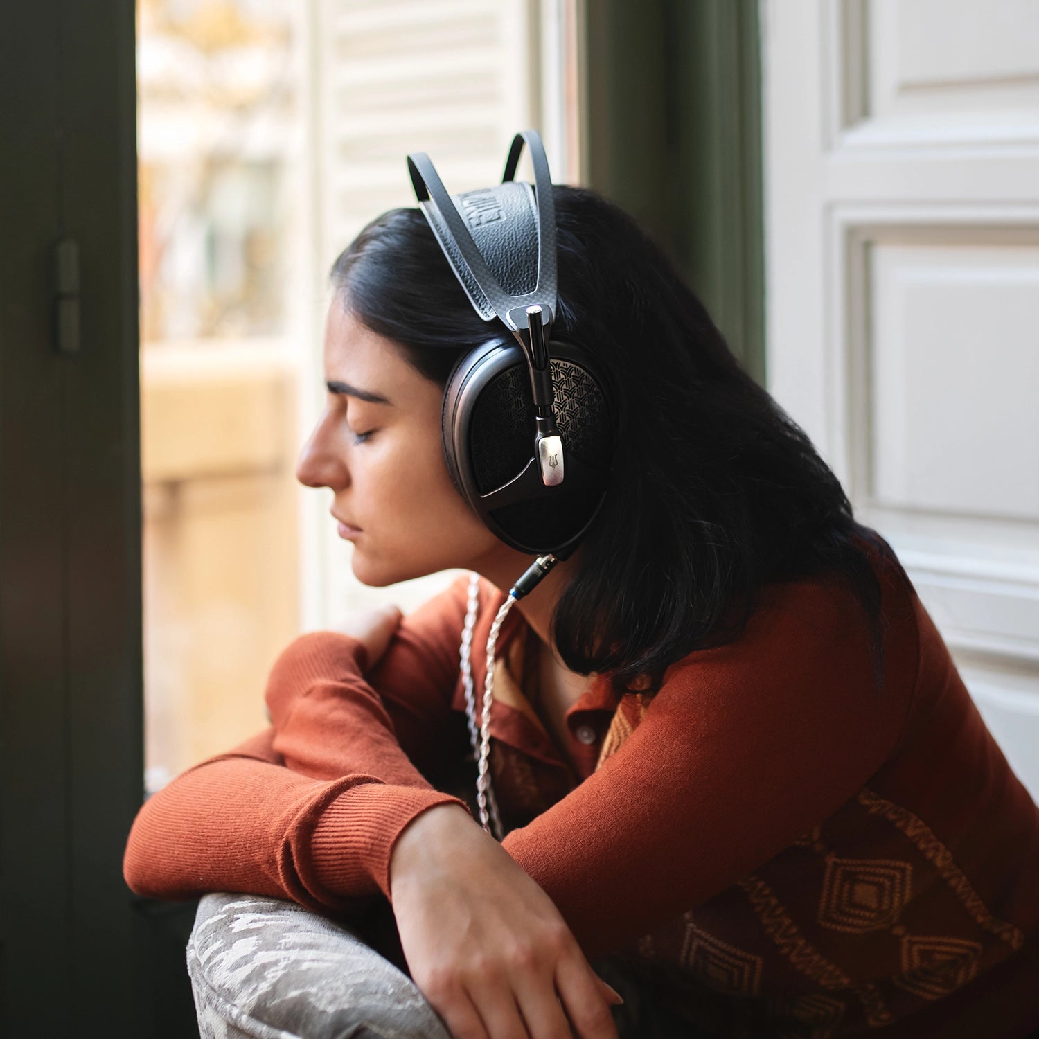 Young woman sitting in her apartment listening to music on her Meze Audio Empyrean II planar wired head phones