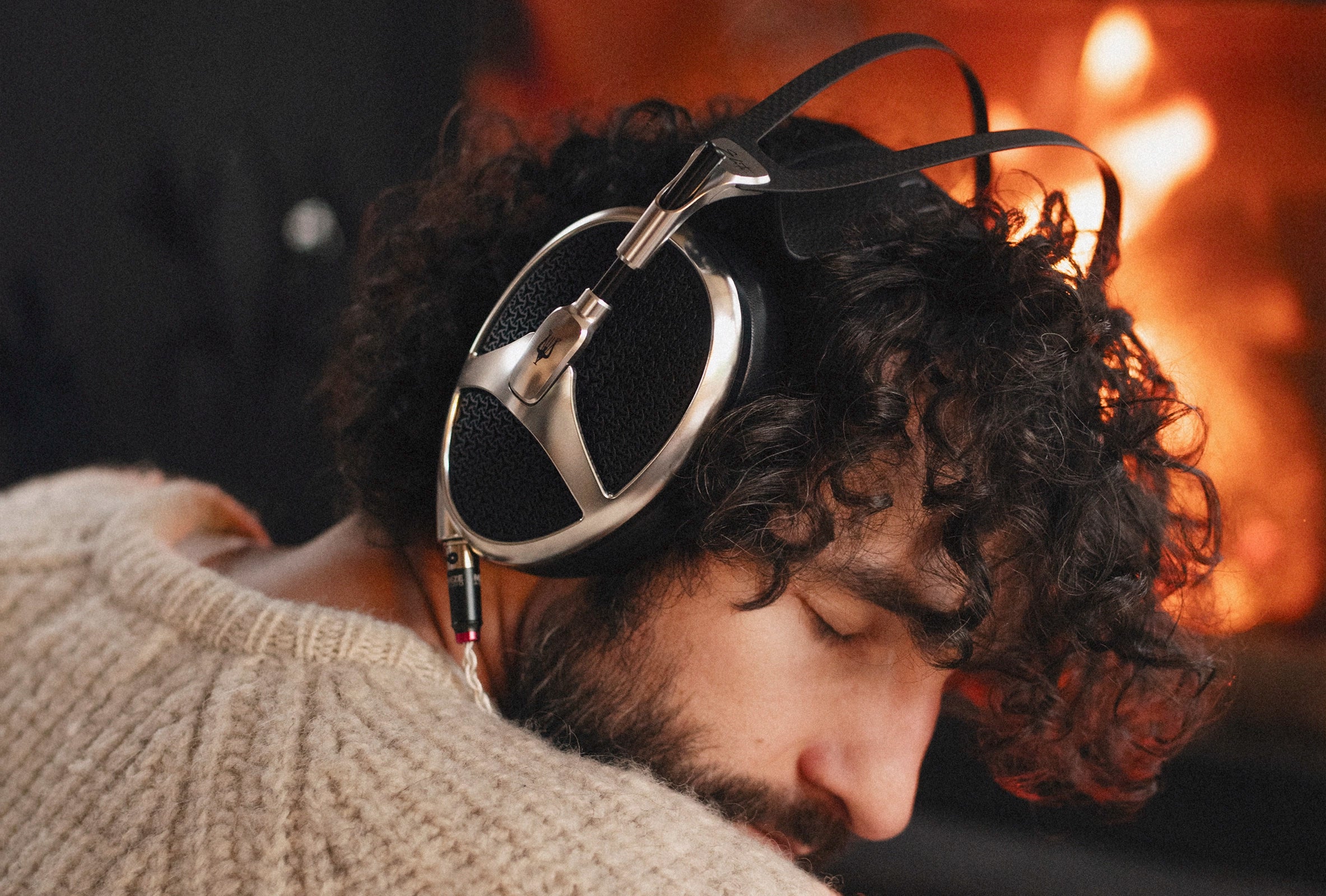 Man listening in front of the fireplace to  Meze Audio Elite Aluminium planar magnetic open back audiophile headphones